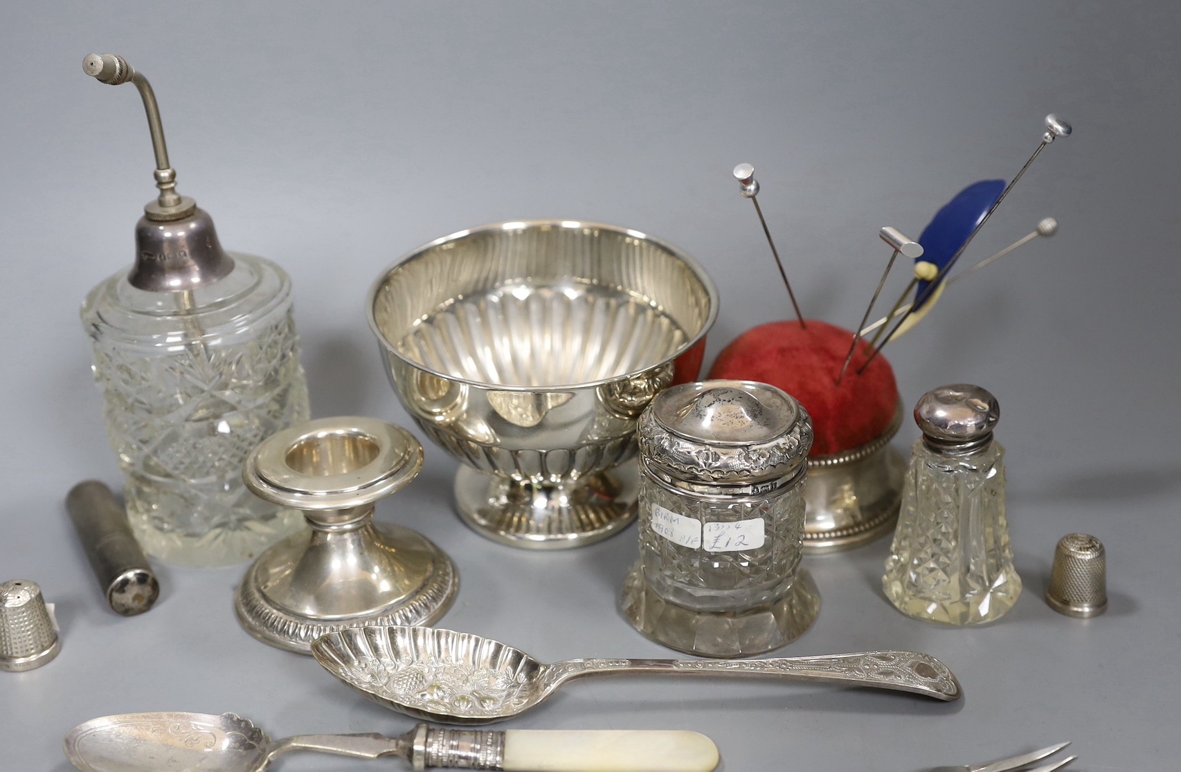 Small silver items including 800 standard dwarf candlestick, a George V silver mounted pin cushion, a silver mounted glass atomiser and two toilet jars, a sterling lighter, two silver thimbles, four items of silver flatw